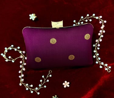 Elegant purple silk clutch bag with gold embroidery on red velvet, featuring floral jewelry accents.