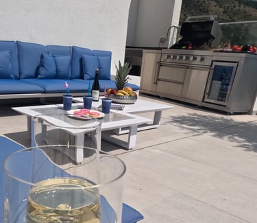 Villa Fay outdoor lounge with a glass of wine on a patio with a blue couch and outdoor kitchen BBQ