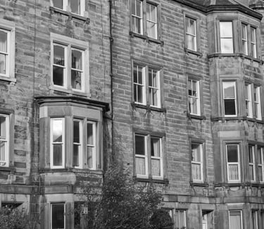 A black and white photo of a traditional stone tenement building featuring bay windows.