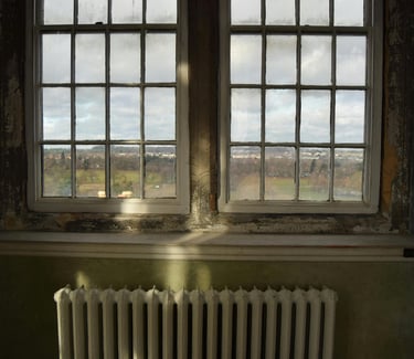 Vintage white radiator sitting below large multi-pane windows 