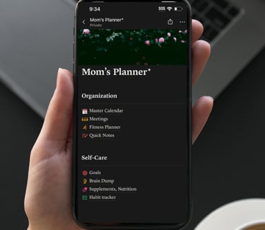 A person holding a smartphone displaying a digital Mom's Planner app with organization and self-care schedules.