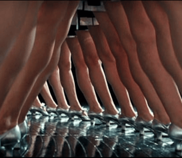 Homage scene from Ken Russell’s The Boy Friend (1971) with silver‑shoed dancers in wide‑leg stance.