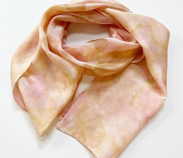Light pink and beige silk scarf with a soft watercolor-style pattern, loosely folded on a white background.
