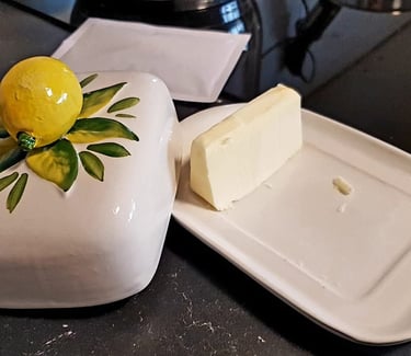A stick of fresh butter on a white ceramic butter dish with a decorative lemon-topped lid.