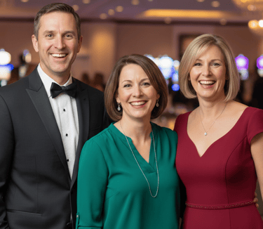 group of 3 people, 2 women wearing a red dress and a green dress and one man wearing a tuxedo