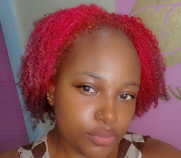 A young woman with rosy pink natural curls, styled in a short, voluminous shape. Her glowing skin, subtle makeup, and nose pi