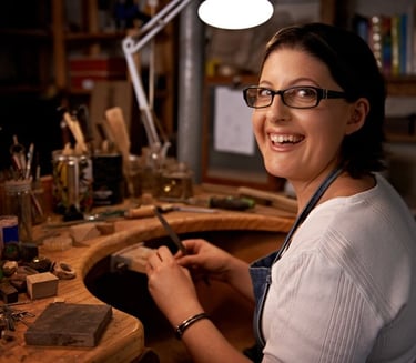 Joyera artesana sonríe mientras usa sus herramientas en un banco de un taller de joyería