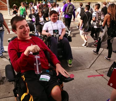 Two young men in power wheelchairs smiling as another group of people walks away from camera