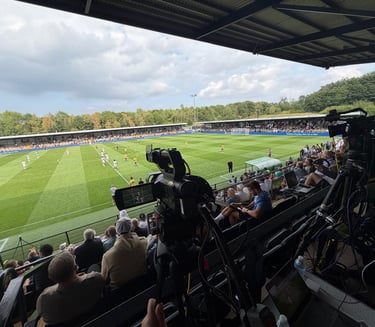 Professional broadcast cameras filming a live soccer match at a crowded stadium from the press box.