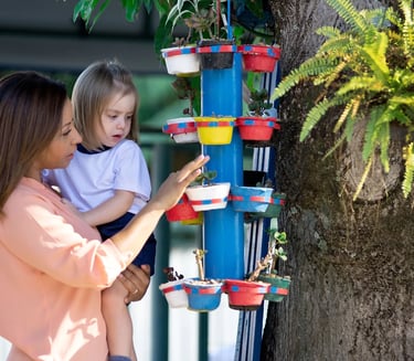 Teacher showing a toddler a vertical garden with colorful planters during an outdoor learning activi