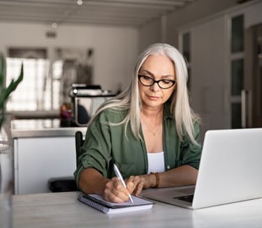 a woman in glasses and a green shirt is sitting at a desk with a notebook