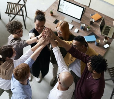 A group of people in an office, hands raised, ready to assist.