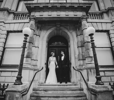 Black and white photo of bride & groom standing at a grand building entrance,captured by Fred Studio