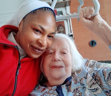 A smiling caregiver and an elderly woman holding a bed trapeze handle during home elder care.