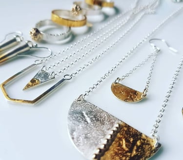 Handmade mixed metal jewellery including silver and gold geometric necklaces, rings, and earrings.