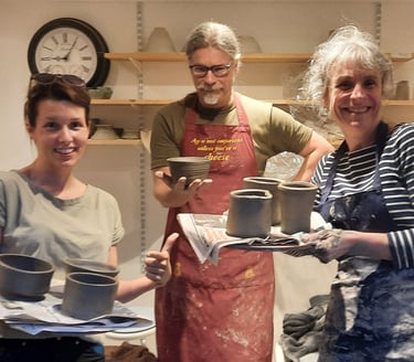 three people standing holding the pots they threw on the beginners course
