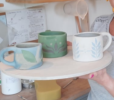 a smiling woman holding three mugs she threw and decorated on the improvers course