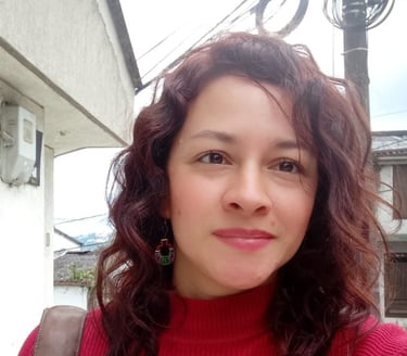 Una mujer con cabello ondulado color castaño rojizo, usando un suéter rojo de cuello alto y aretes .