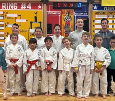 A youth karate tournament group standing in front of competition brackets and a scoreboard in Altoona, PA.