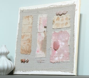 Abstract textile artwork on canvas with irregular stitched fabric in muted beige, pink, and gray tones with rose quartz stone