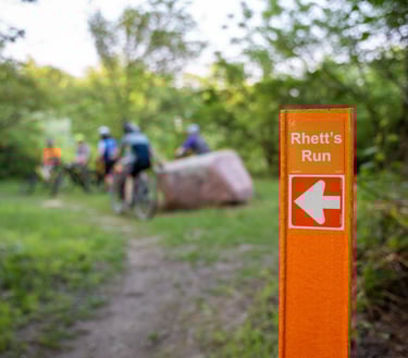 Group of bikers in the background of a focus shot on the "Rhett's Run" signange