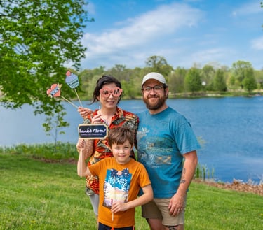 Staged photo of a couple with a young child in front of a lake, holding up paper props