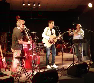 Joël Royer au centre de la scène joue de la guitare sèche avec contrebasse et flûte traversière