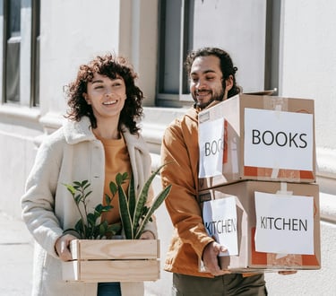 Couple walking together carrying moving boxes and house plants