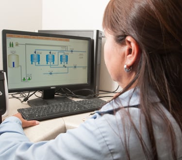 A technician monitors a water filtration system on a desktop computer in an office setting.
