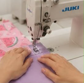Una persona utiliza una máquina de coser industrial Juki blanca para coser una tela con estampado.