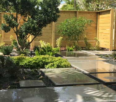 Modern garden landscape with concrete paver walkway, lush green plants, and a horizontal wood fence.