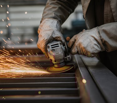 عامل يقوم بقطع وصقل معدن الستانلس ستيل داخل ورشة صناعية ضمن عمليات تصنيع معدات المطابخ والمطاعم.