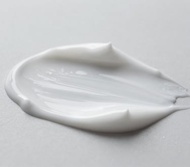 Macro shot of a cosmetic cream texture being gently spread, highlighting its smooth and even consistency, clean neutral studio lighting, cool desaturated tones, sharp focus, shallow depth of field, clinical aesthetic