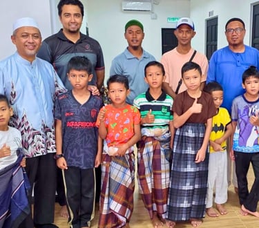 A group of young boys and men posing together indoors wearing traditional sarongs and casual clothing.