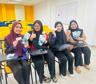 Four smiling female students in hijabs hold health awareness brochures in a modern university classroom.