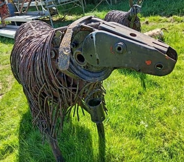 Rustic metal sheep sculpture crafted from recycled farm tools and wire standing in a green field.