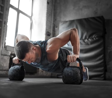Athletic man performing kettlebell pushups for strength training in a rustic industrial gym.