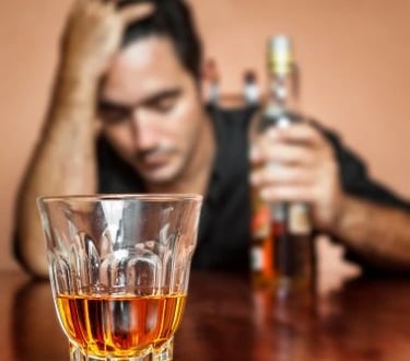 homme 1 bouteille d'alcool à la main gauche main droite sur la tête et verre devant lui presque vide