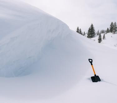 Winter wilderness shelter prep with untouched snow pile and survival shovel before constructing quinzee or snow cave