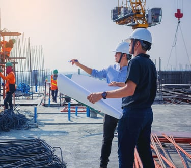 two men in hard hats and safety vests standing in front of a building