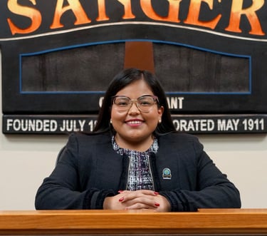 a woman in a black jacket and glasses sitting at a podium