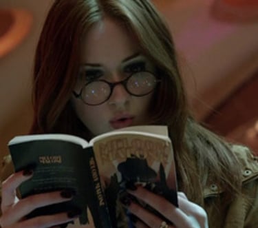 a woman in glasses and a jacket is reading a book