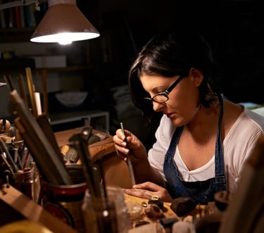 Artesana joyera elaborando joyería hecha a mano con herramientas de precisión en un taller.