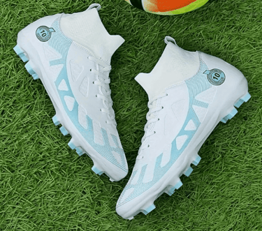 Botines de fútbol de caña alta en blanco y azul claro con tacos para terreno firme sobre césped.