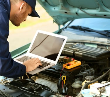 A professional mechanic uses a laptop to perform a digital car engine diagnostic for vehicle repair.