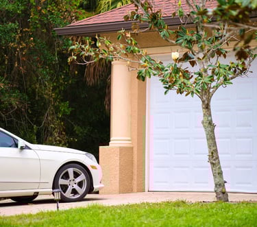 White sedan parkedo on a paved driveway in front of a modern home with a white sectional garage dor.