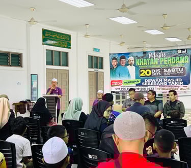 A community meeting at Dewan Masjid Seberang Takir with a speaker at a podium addressing an audience.