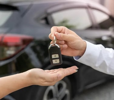 A person handing over electronic car keys to a new owner in front of a black SUV.