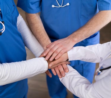 Profesionales médicos con las manos juntas, simbolizando el trabajo en equipo y la colaboración