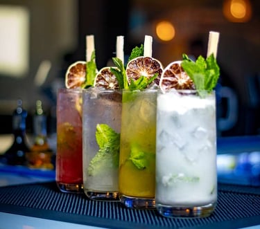 Variety of colorful mojito cocktails with fresh mint and dried lime garnishes on a bar mat.